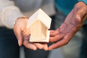 Close-up of hands holding a small wooden house, representing real estate and new home ownership.